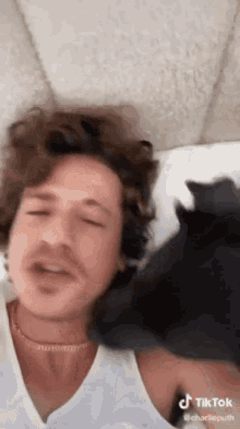 a man is laying on a bed with a black cat on his shoulder .