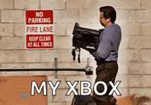 a man is carrying a camera in front of a no parking fire lane sign