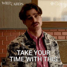 a man with a mustache is standing in front of a brick wall and says " take your time with this "