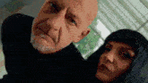 a bald man with a beard and a woman with long black hair are looking at the camera .
