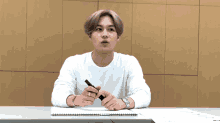 a young man sitting at a desk holding a pen
