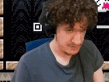 a man with curly hair wearing headphones is sitting in front of a pixelated background .