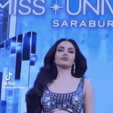 a woman in a crop top is standing in front of a sign that says miss universe saraburi .