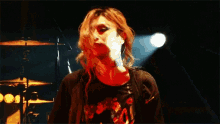 a woman in a red shirt is standing in front of a drum set on a stage .