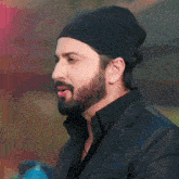a man with a beard wearing a black beanie and a black suit .