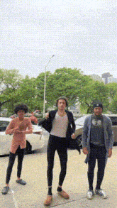 three young men are standing on a sidewalk in front of a white car .