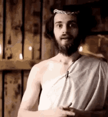 a man with a beard and a toga is wearing a crown of thorns and looking at the camera .