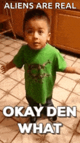 a little boy in a green shirt is standing on a tiled floor and making a funny face .