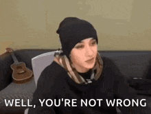 a woman is sitting on a couch wearing a beanie and a scarf .