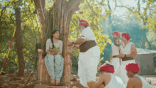 a group of people are standing around a tree with a woman sitting in the middle