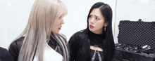 two women are standing next to each other and looking at each other in front of a suitcase .