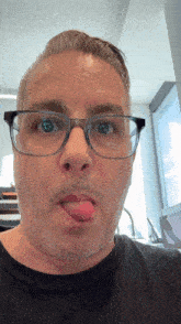 a man wearing glasses and a black shirt sticks his tongue out