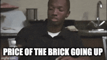 a man is sitting in a kitchen with the words price of the brick going up written on the screen .
