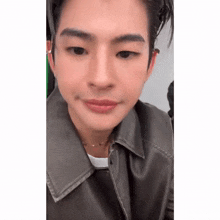 a close up of a young man wearing a leather jacket and necklace .