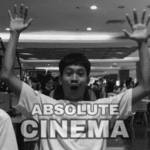 a man in an absolute cinema t-shirt holds his hands up in the air