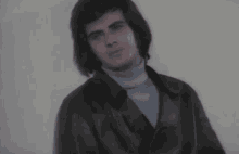 a man in a leather jacket and turtleneck looks at the camera