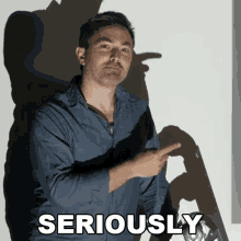 a man in a blue shirt is pointing at something with the word seriously above him