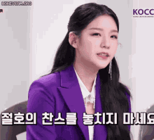 a woman in a purple suit is sitting in front of a kocc logo .