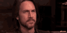 a man with a beard is making a funny face while holding his finger to his face .