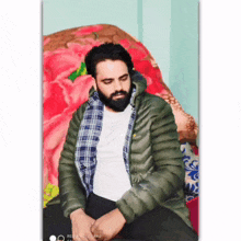 a man with a beard is sitting on a couch with a blanket behind him .