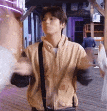 a young man in a tan jacket is standing on a wooden deck .