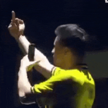 a man in a yellow shirt is holding a microphone and giving a middle finger .