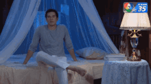 a man sits on a bed next to a lamp that says 35 on it