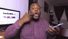 a man in a plaid shirt is holding a cell phone and making a funny face