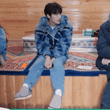a man in a blue jacket is sitting on a wooden bench with his legs crossed .