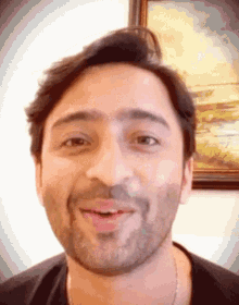 a man with a beard is smiling in front of a framed painting