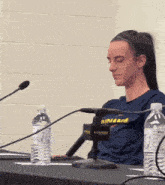 a woman wearing a shirt that says indiana sits at a table with two water bottles