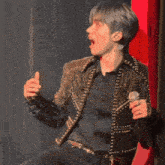 a young man in a studded jacket is holding a microphone in his hand .