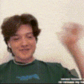 a man in a green shirt is raising his fist in the air while wearing headphones .