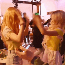 two blonde women are dancing in a room with a green sign that says oi
