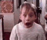 a young boy is making a surprised face while wearing a white sweater .