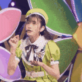 a girl in a green dress and yellow hat is sitting in front of a colorful background