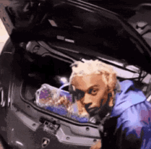 a man is looking into the trunk of a car with his hood open .