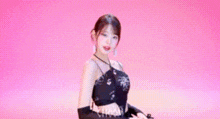 a woman is standing in front of a pink background wearing a black dress and gloves .