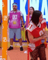 a man wearing a pink jersey with the number 03 stands next to a woman wearing a red jersey with the number 7