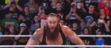 a man with a beard is standing in a wrestling ring with his arms up in the air .