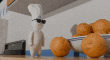 a pillsbury dough boy wearing sunglasses and a chef 's hat stands in front of a bowl of oranges