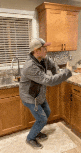 a man in a gray jacket and hat is squatting down in a kitchen