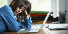 a woman laying on a desk with her head resting on a laptop computer