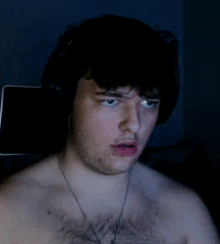 a shirtless man wearing headphones and a necklace looks surprised