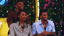 three men are sitting next to each other in front of flowers