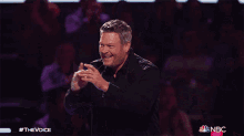 a man in a black shirt is laughing and pointing at the camera with a nbc logo in the background