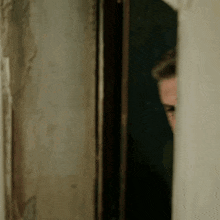 a man is peeking out of a doorway and looking at the camera .