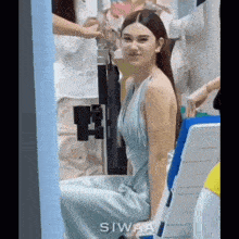a woman in a blue dress is sitting on a chair and looking at the camera .