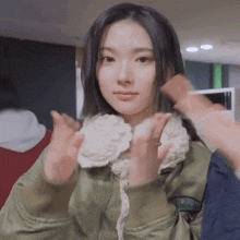a young woman in a green jacket is making a peace sign with her hands .