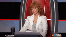 a woman in a white jacket sits in a chair with a nbc logo in the background